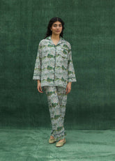 A women wearing a green silk pajama set with floral prints, consisting of a button-down shirt and matching pants.